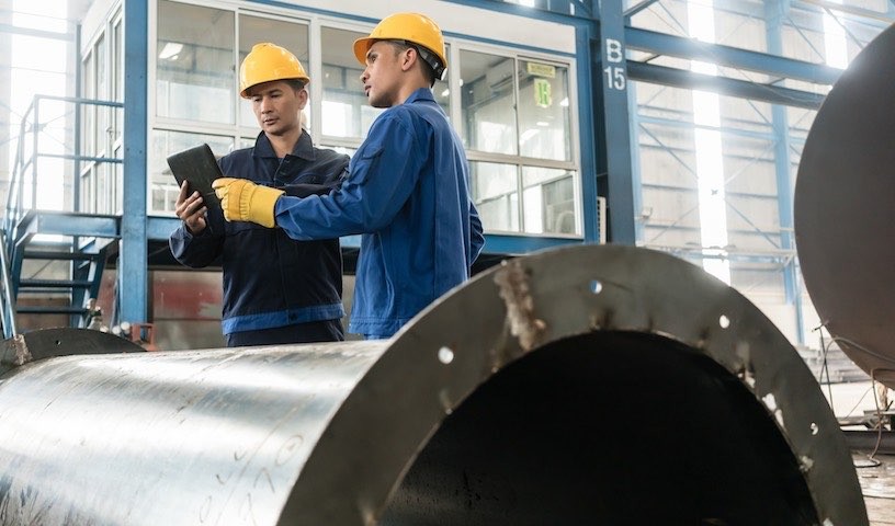 Asian experts checking information on tablet PC while supervising work in a modern factory